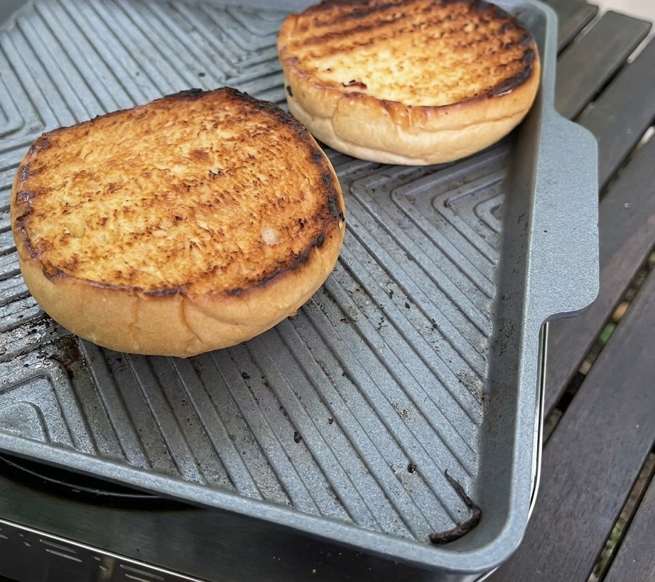 A silver spoon spreading a thick creamy pink sauce over the golden surface of a toasted brioche bun.