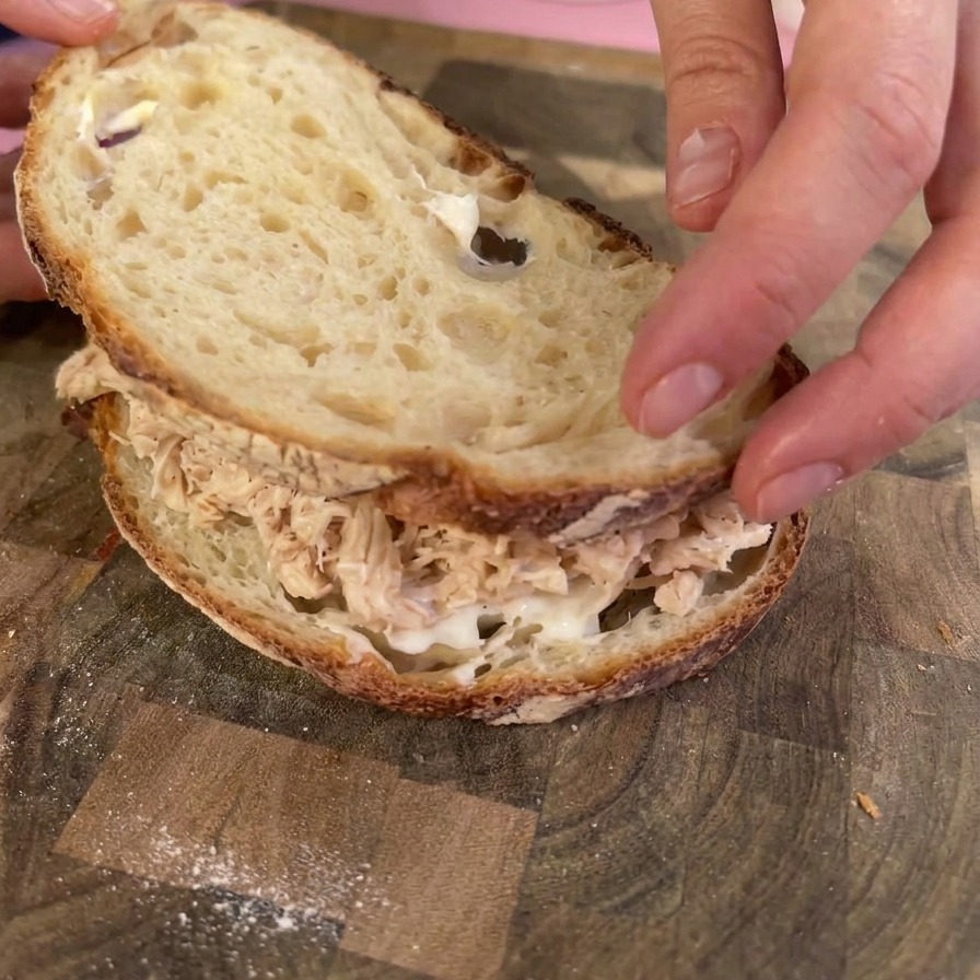 Hands placing a toasted slice of sourdough bread on top of a heap of shredded chicken to close the sandwich.