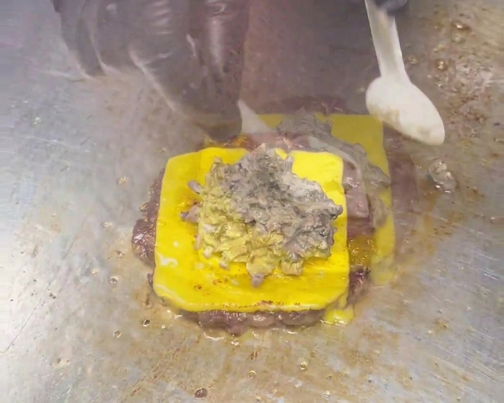 A spoon spreading a thick, creamy grey-brown mushroom sauce over a cheeseburger patty.