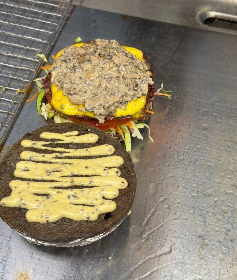 A stack of sliced sautéed mushrooms resting on a burger patty assembled with cheese and sauce.