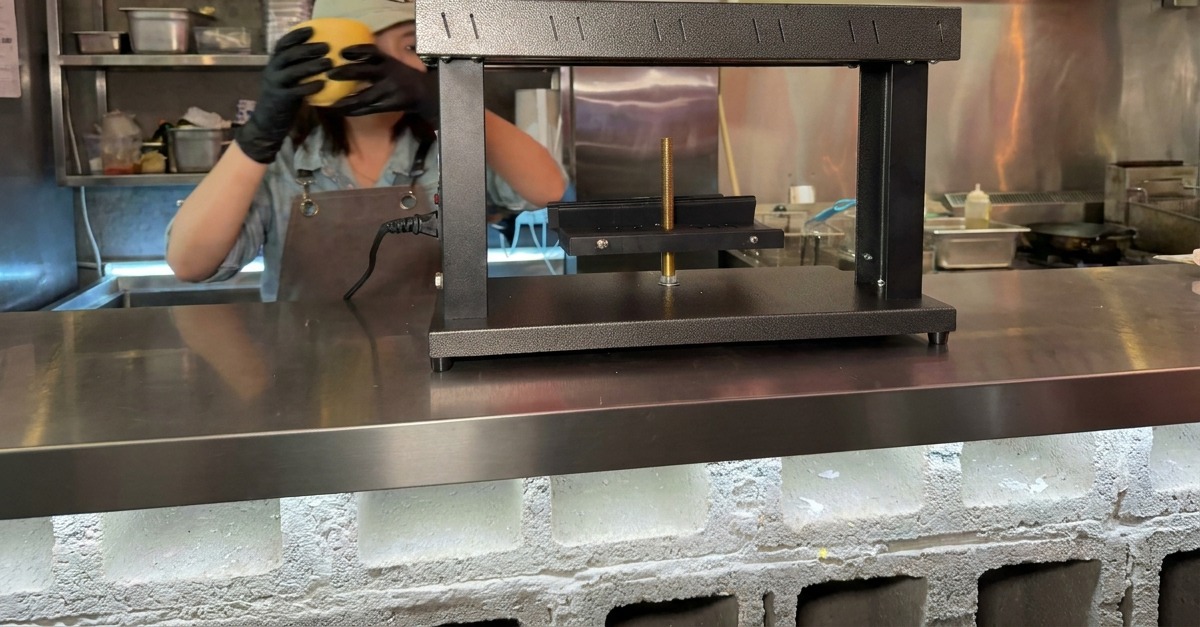 Hands placing a semi circular block of cheese onto the base of a specialized melting machine