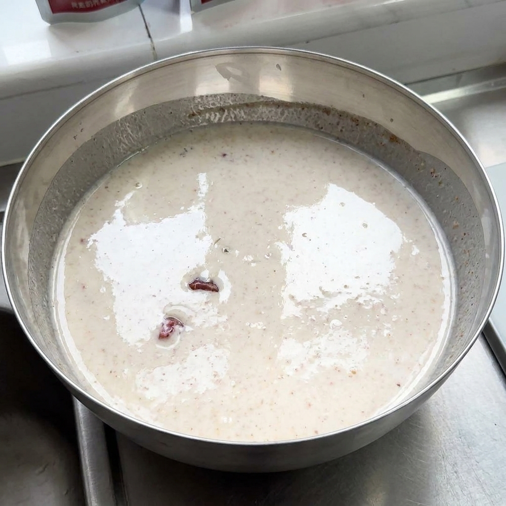 Raw chicken pieces resting inside a large metal bowl filled with a creamy, spiced yogurt marinade.