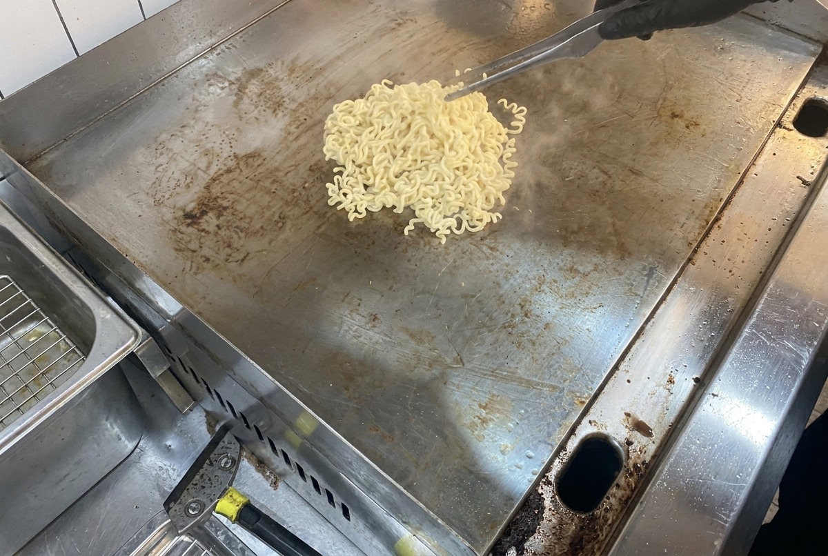A view of steaming noodles and melting butter on a large flat metal cooking surface.