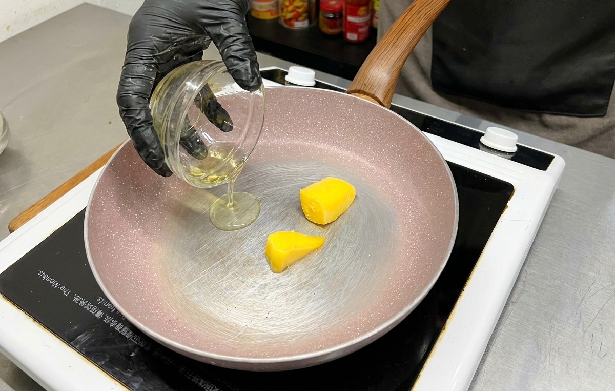 Two blocks of yellow butter sitting in a frying pan as olive oil is poured in from a glass bowl.