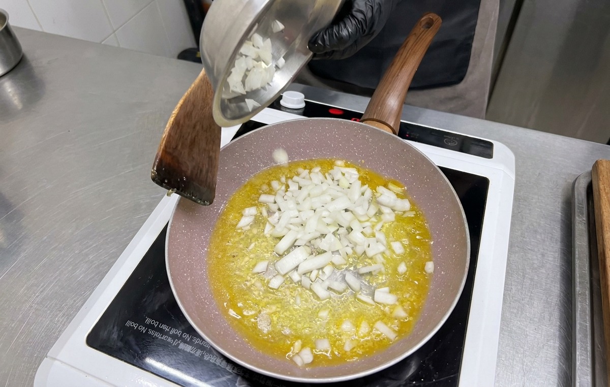 Diced white onions being poured from a metal bowl into the frying pan over the garlic and butter.