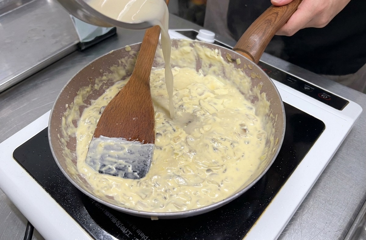 Clear broth being poured from a stainless steel bowl into a pan of simmering mushrooms and cream.