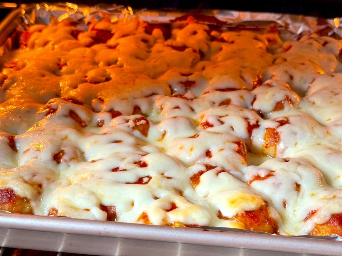 A close-up view of thick white cheese bubbling and browning over food inside a glowing oven.