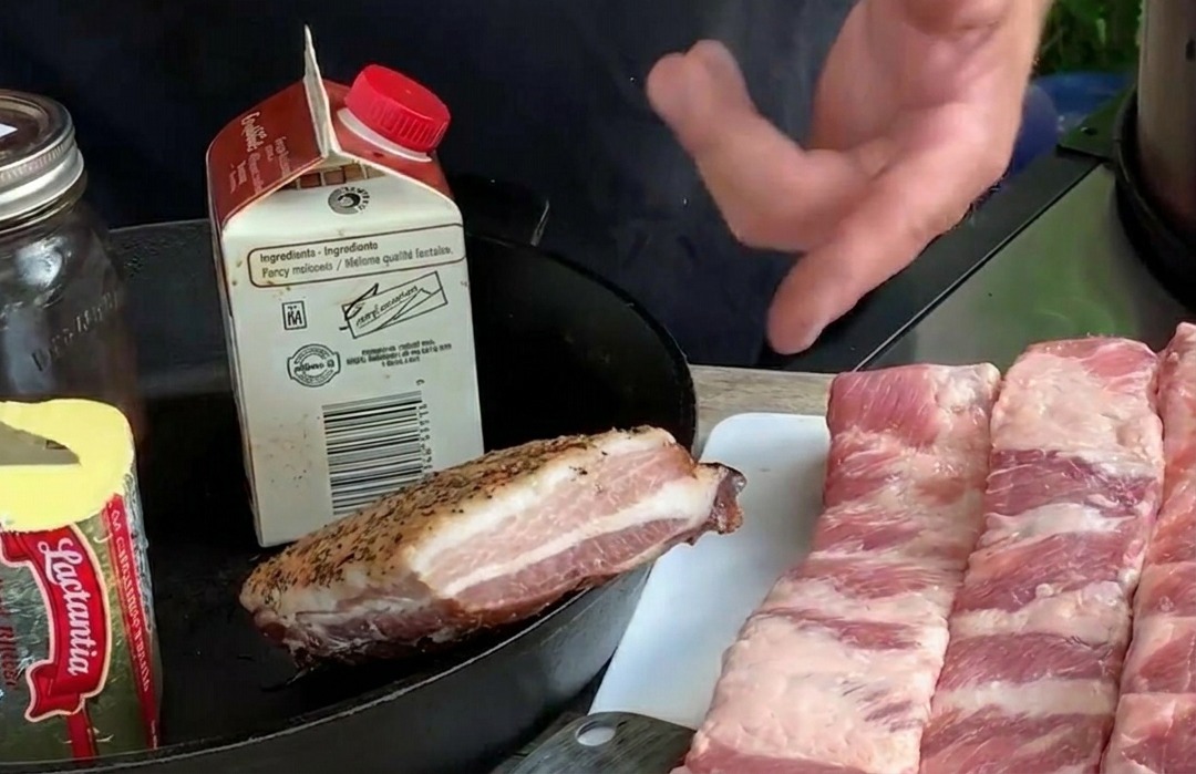 Several long raw pork rib strips laid out on a white cutting board alongside ingredients like butter and fresh blueberries.