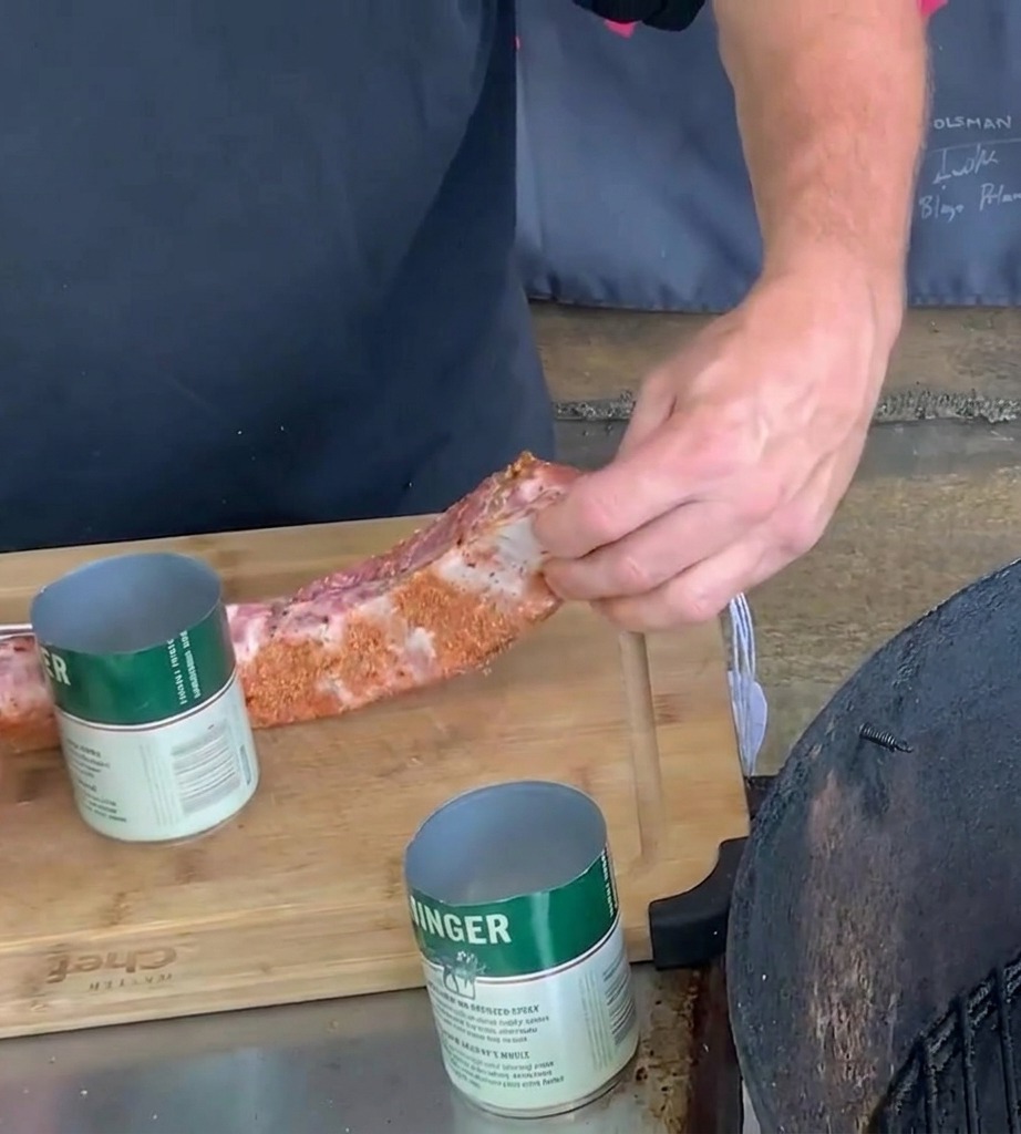 A pair of hands wrapping a spice rubbed pork rib around a green and white metal beer can on a wooden cutting board.