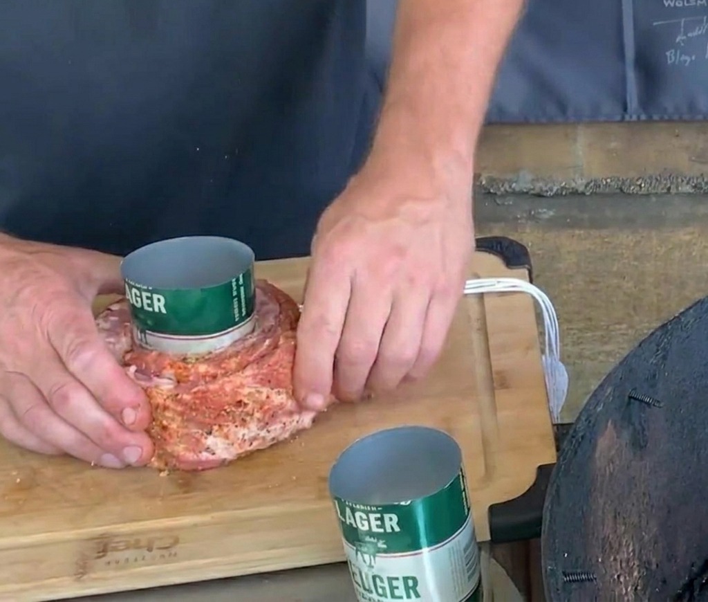 Hands carefully securing white twine around a seasoned pork rib wrapped around a green beer can.