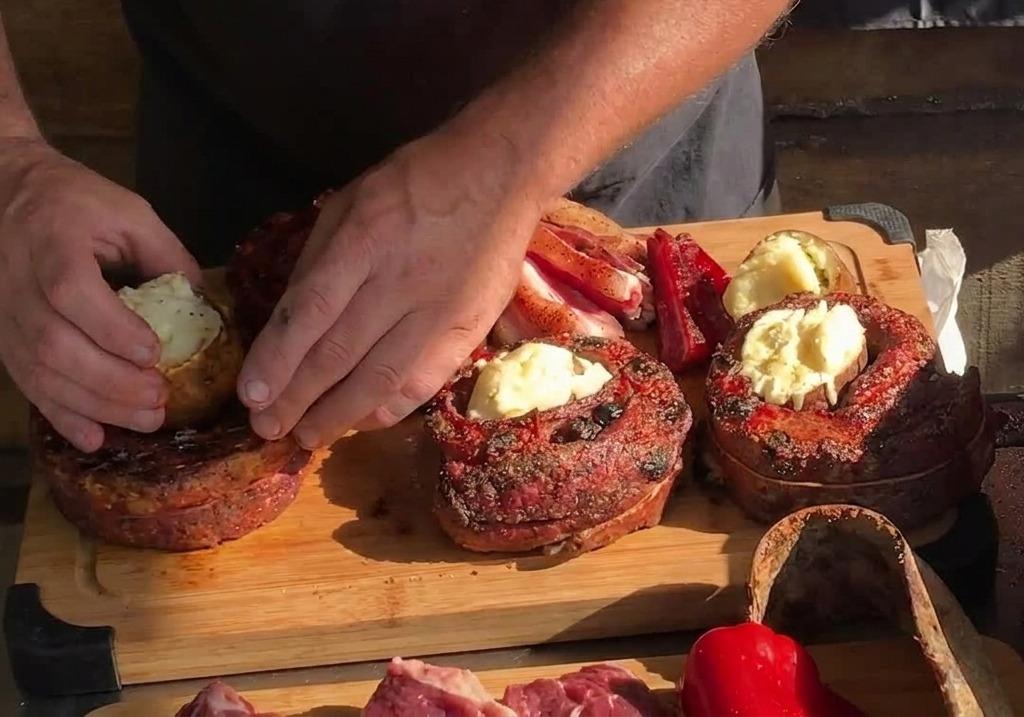 Hands placing a whole roasted potato into the hollow center of a cooked, circular rib strip on a wooden board.