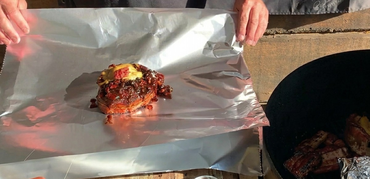A finished BBQ rib cup topped with melted cheese sitting on a large sheet of aluminum foil, ready to be wrapped.
