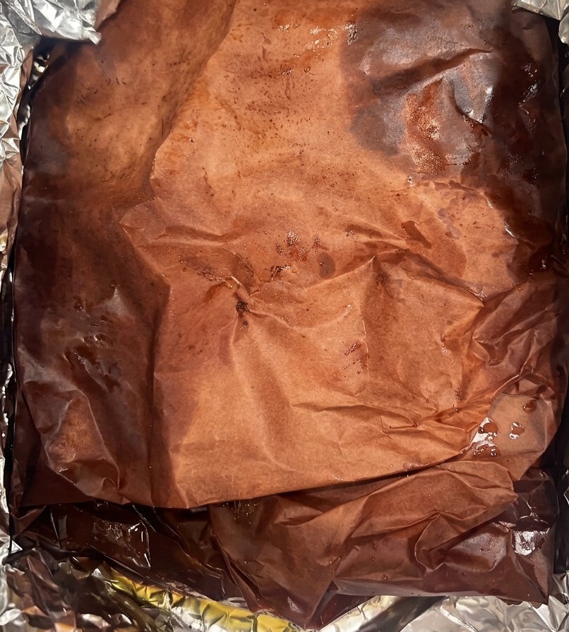 A large brisket wrapped in dark, juice-soaked peach butcher paper sitting inside a foil-lined container.