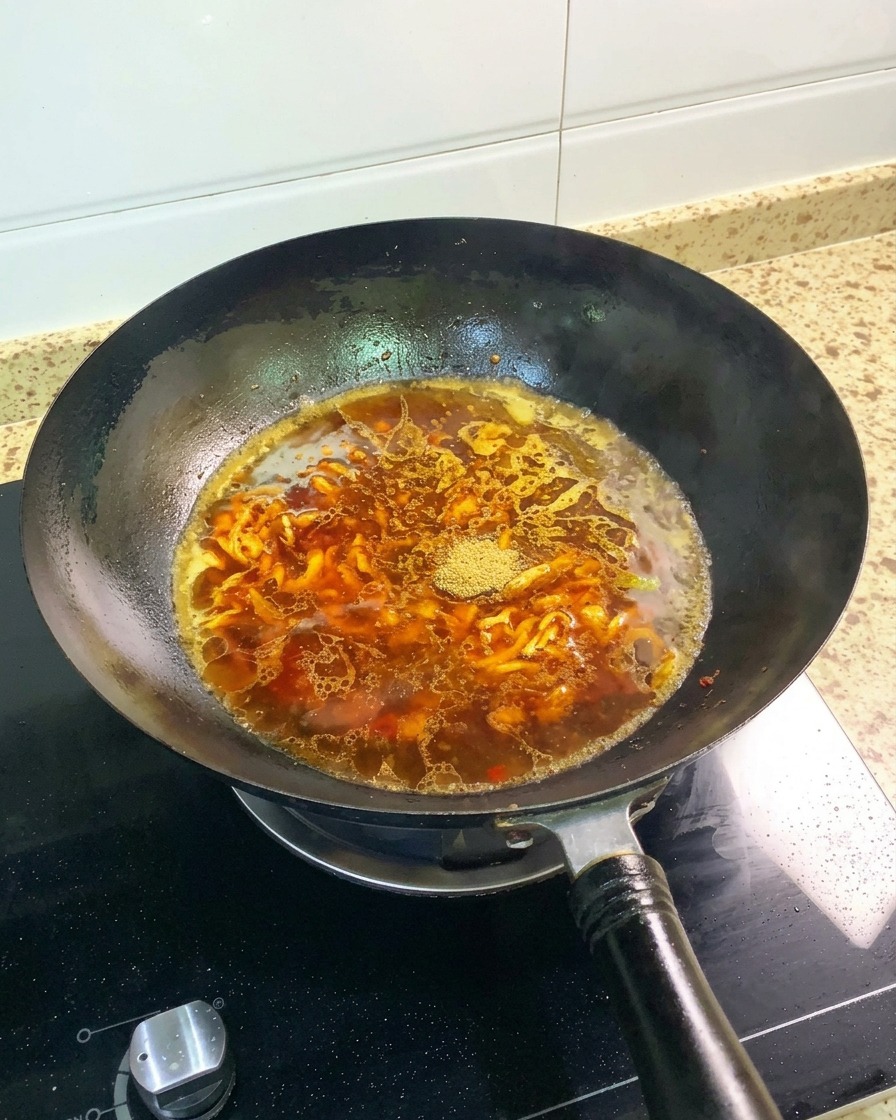 Five-spice powder and a whole star anise sitting on top of the reddish-brown broth in a black wok.