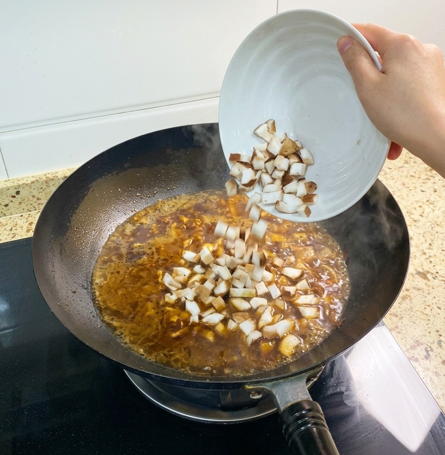 A handful of diced shiitake mushrooms being added to the simmering reddish brown broth in a wok
