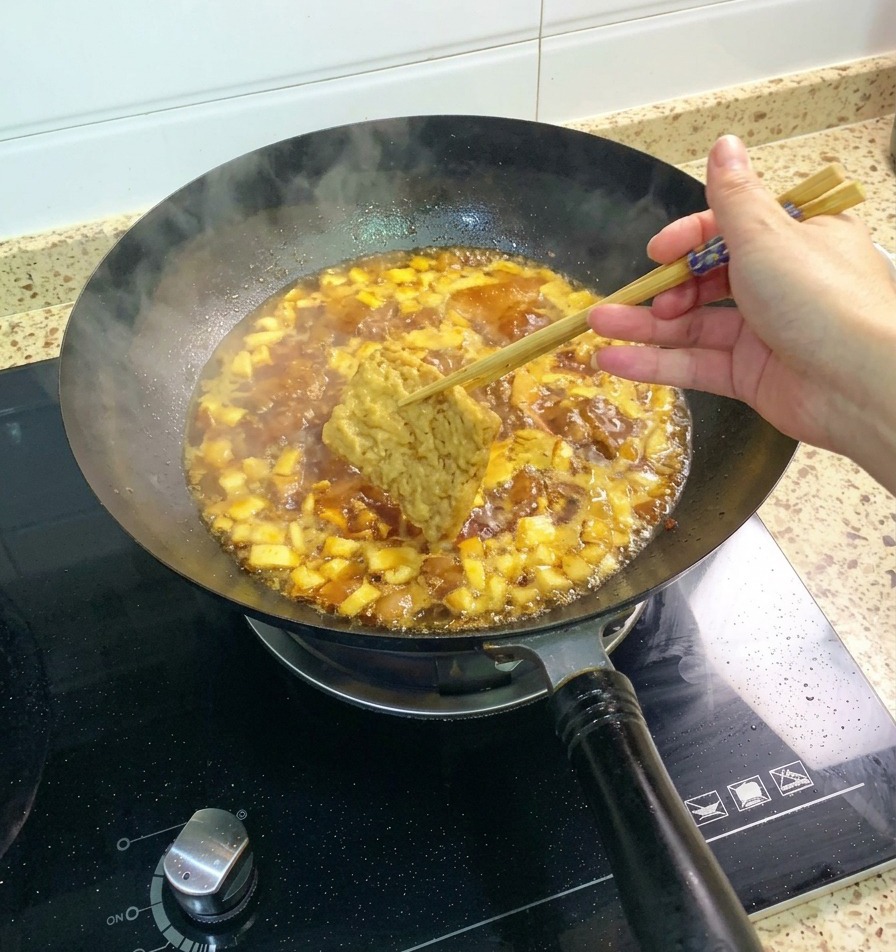 A piece of fried tofu being held by chopsticks and dipped into the bubbling chicken and mushroom sauce.