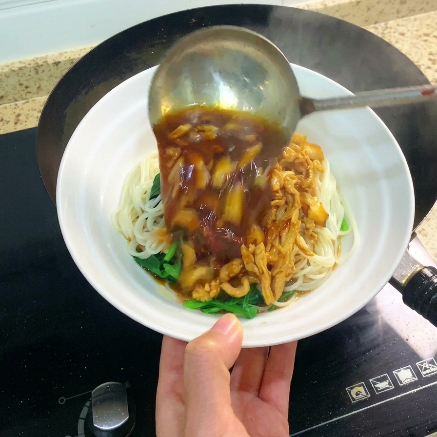A large metal ladle pouring dark, savory shredded chicken and mushroom sauce over a white bowl of noodles.