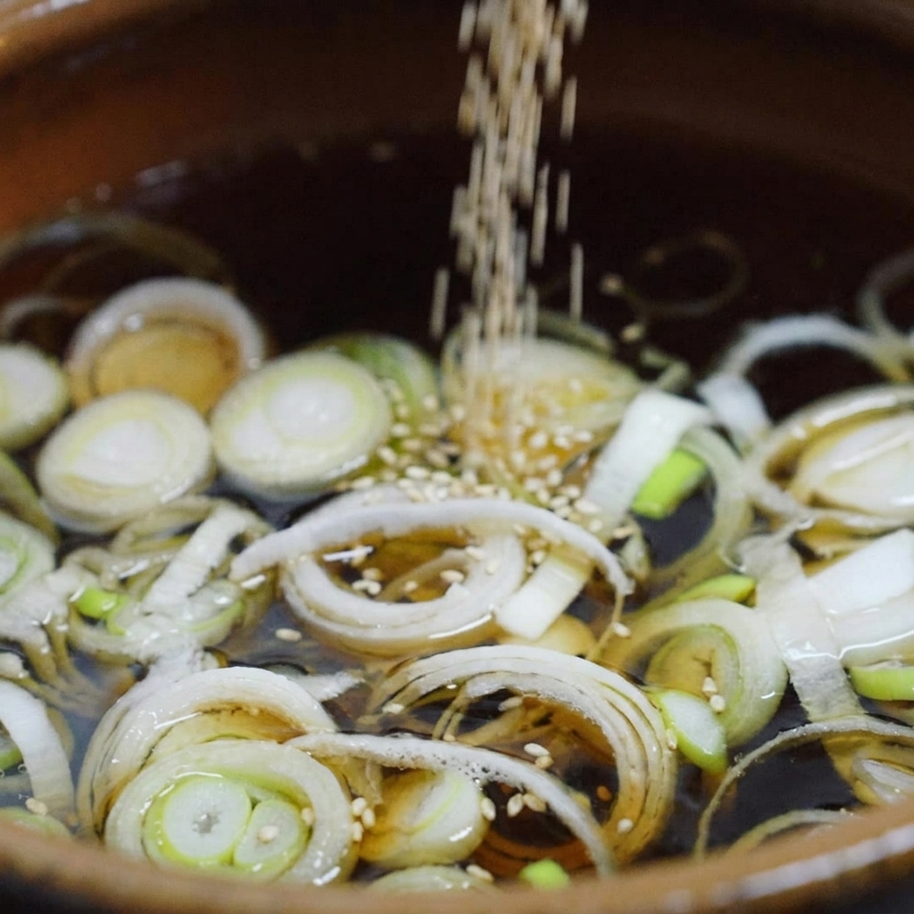 White sesame seeds falling into a dark simmering broth filled with sliced green onions inside a ceramic cooking pot.