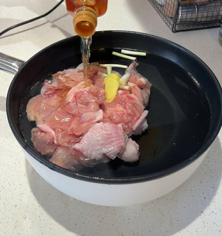 Pouring a clear amber liquid from a glass bottle into the pot of water and chicken.
