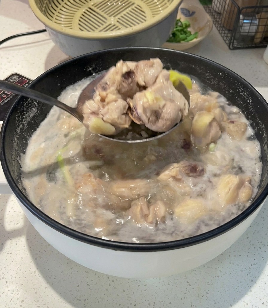 A metal ladle lifting blanched, opaque chicken pieces out of a pot of boiling, foamy water.
