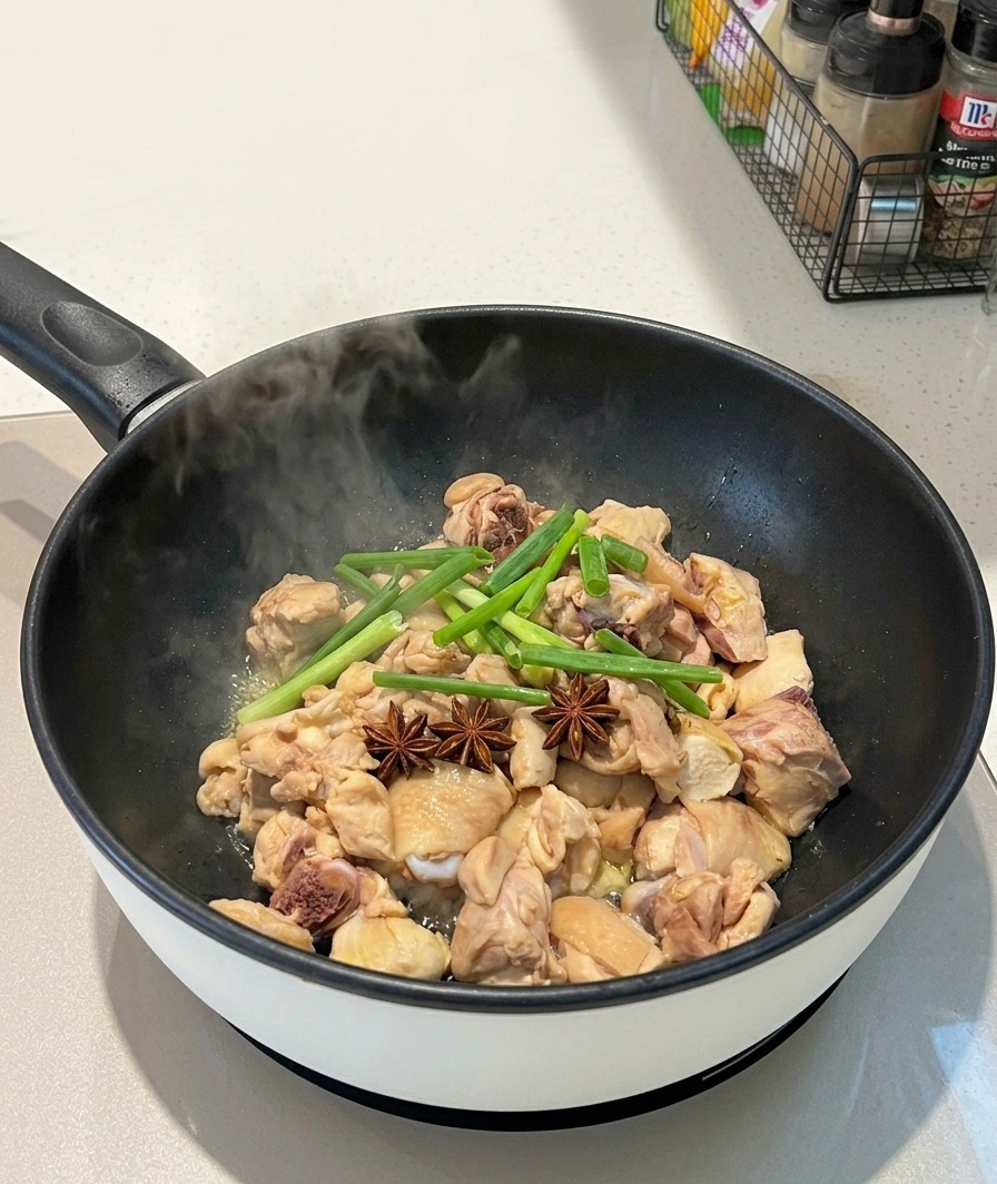 Whole star anise pods and green scallion stalks placed on top of chicken pieces in a steaming pan.