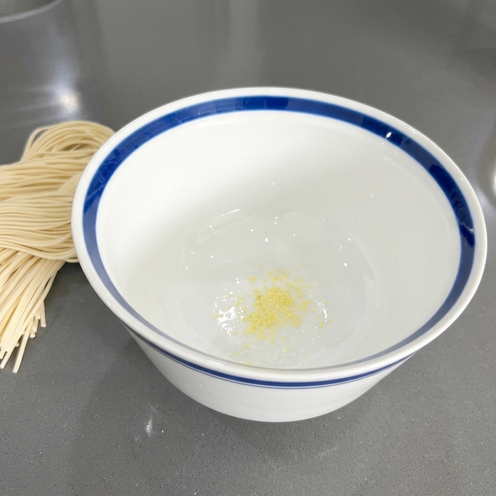 Small yellow-tinted minced garlic pieces sitting at the bottom of a white ceramic bowl.