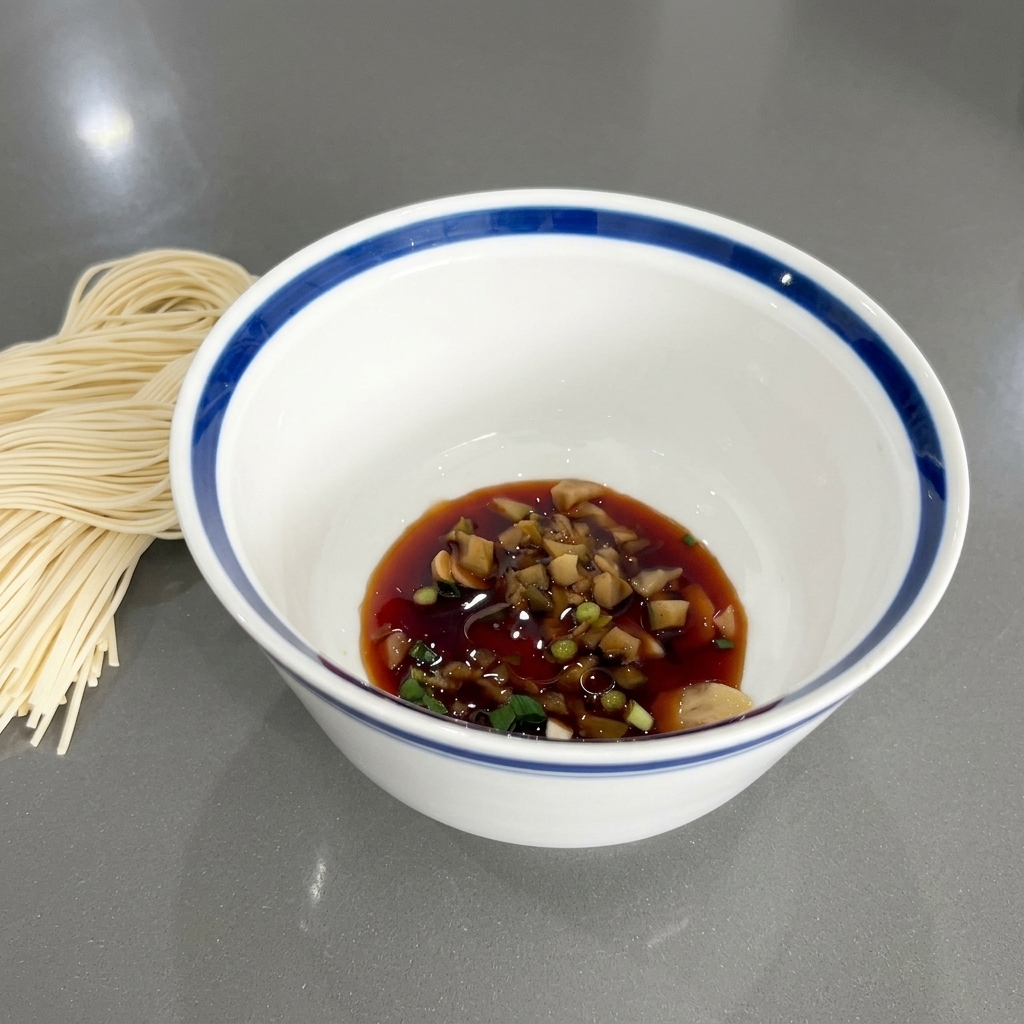 The bowl containing soy sauce, green onions, and aromatics, with a slight sheen from the added sesame oil.