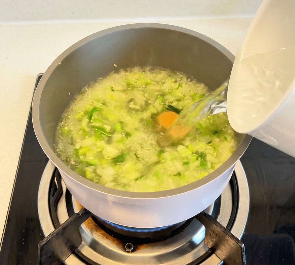 Hot water being poured from a white bowl into a pot filled with vegetables and clear broth.