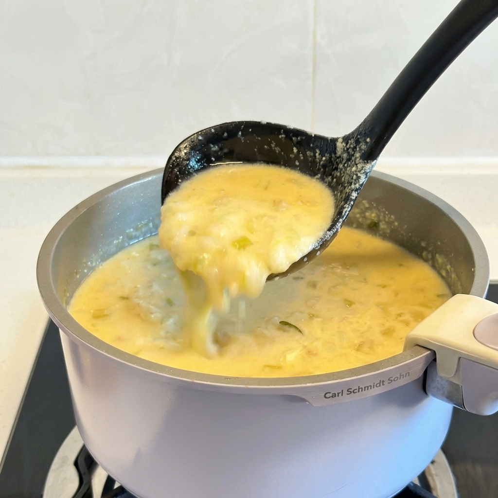 A black ladle lifting a portion of thick, creamy yellow Greek lemon chicken soup from a pot.
