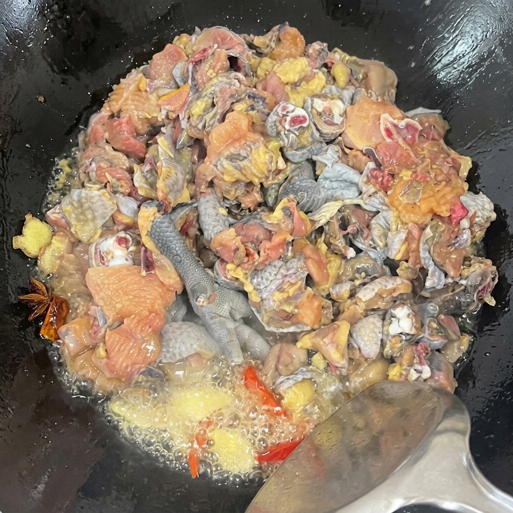 A close-up view of silkie chicken pieces being tossed in a wok with spices, showing the bubbling oil and seasoning process.