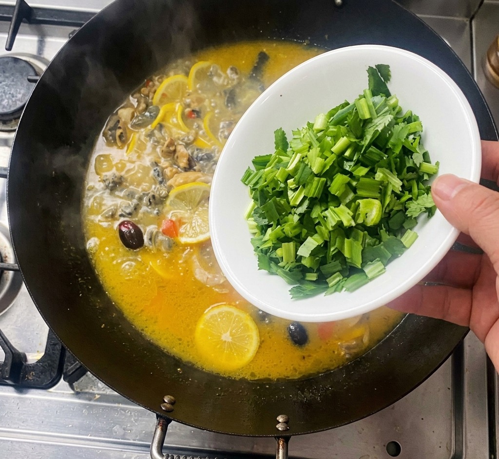 A hand pouring chopped green cilantro from a white bowl into a bubbling wok containing chicken and lemon slices.