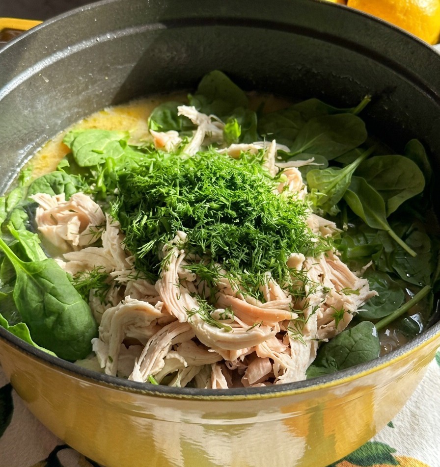 A pot of soup topped with shredded white chicken meat and a large pile of finely chopped fresh green dill.