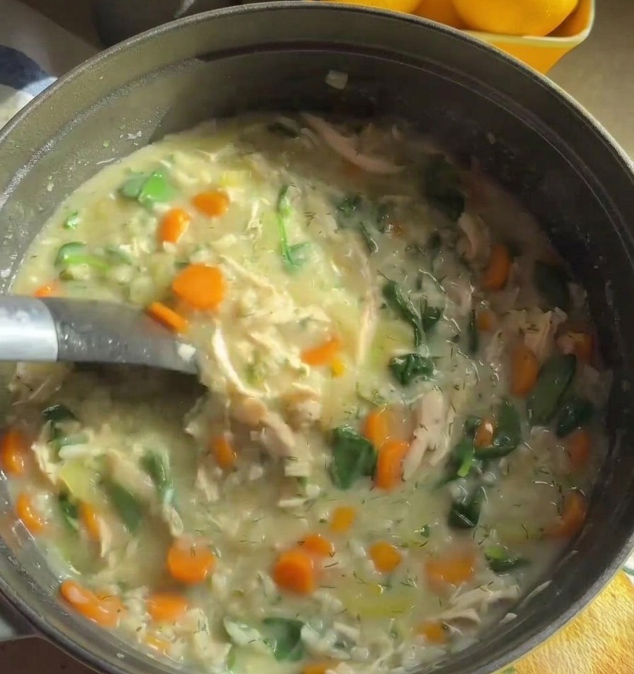 A metal ladle stirring through a thick creamy chicken soup filled with orange carrots and green spinach.