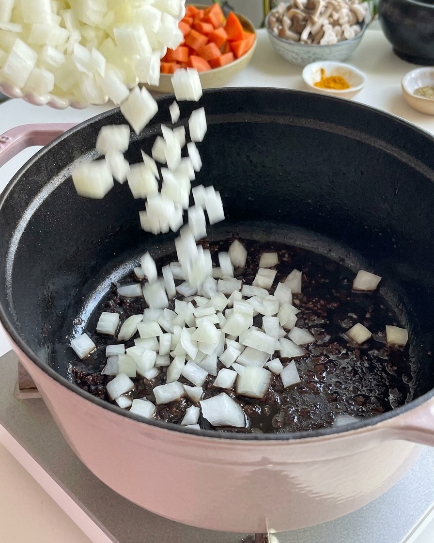 Diced white onions being poured into a cast iron pot to sauté.
