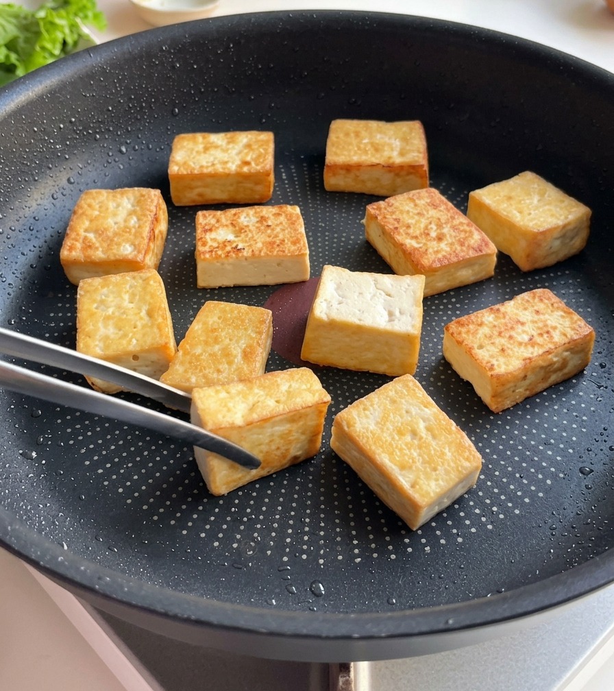 Tofu blocks in a frying pan showing a deep golden brown crust on their cooked surfaces.