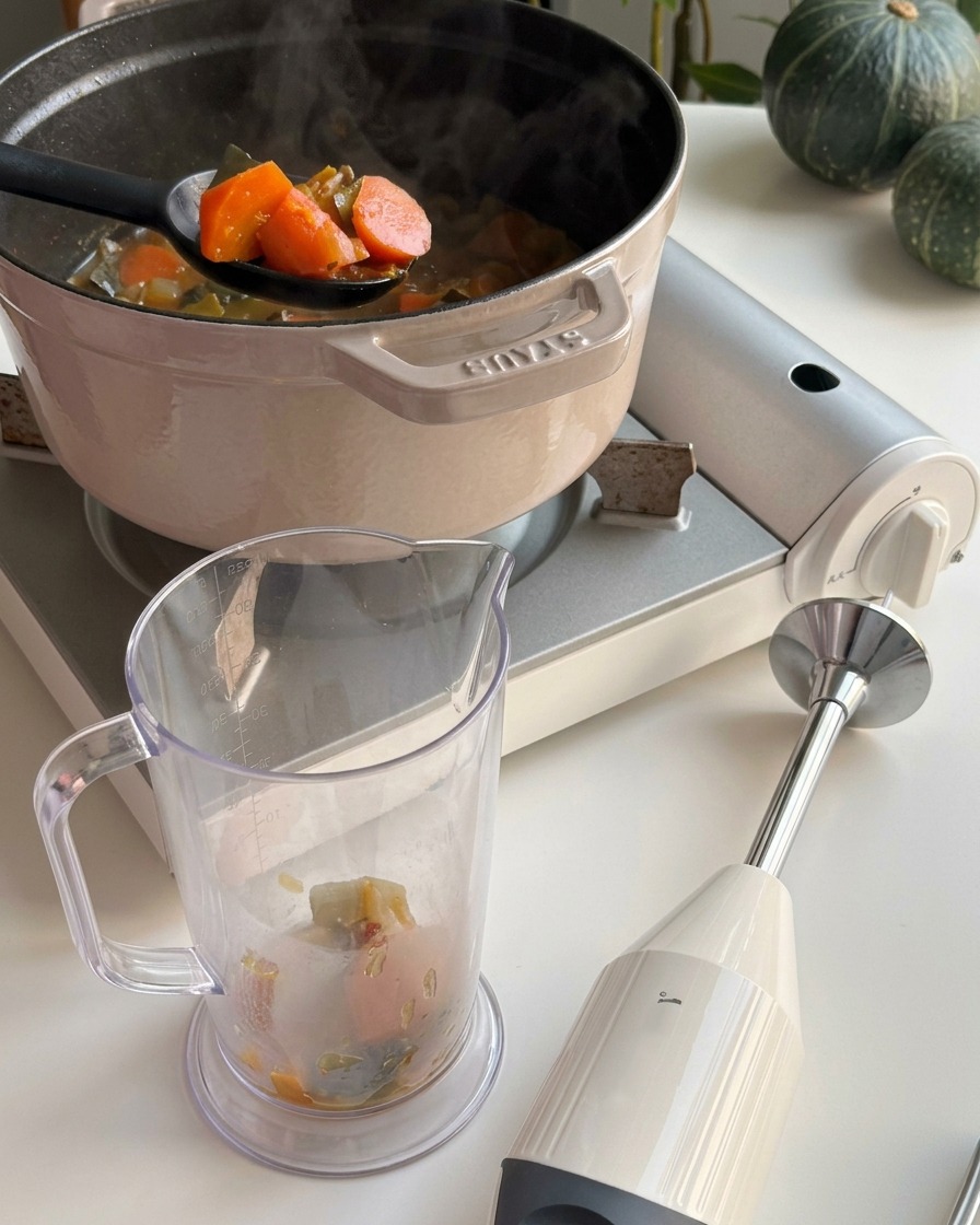 A black ladle scooping orange pumpkin chunks and broth from a pot into a clear plastic blending jar.