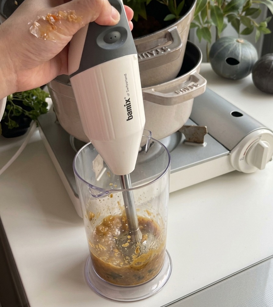 A stream of white coconut milk being poured into a pot of smooth orange pumpkin soup and stirred with a spatula.