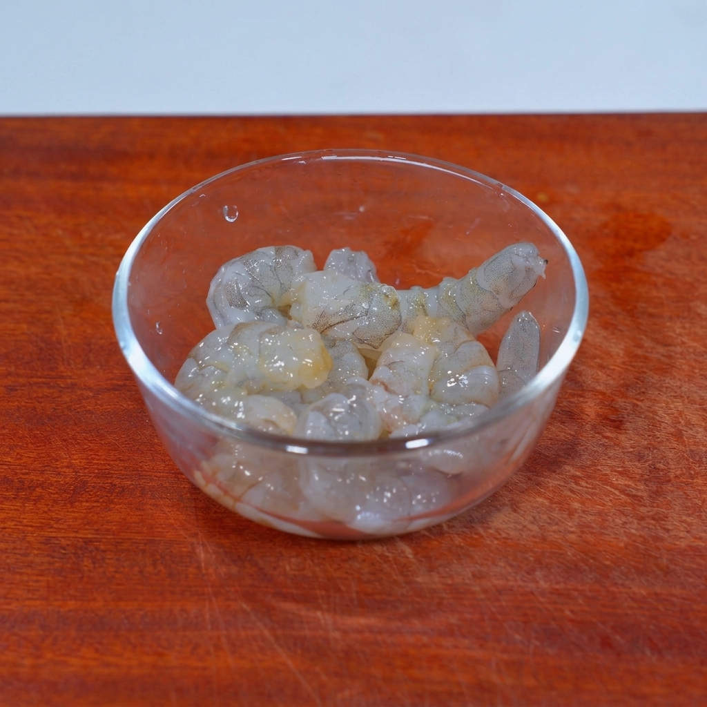 Raw peeled shrimp meat in a glass bowl topped with salt and mushroom seasoning granules.