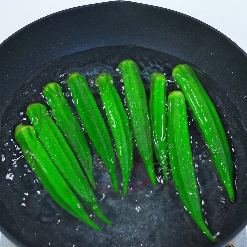 Whole green okra pods submerged in boiling water within a black pot, with small bubbles rising to the surface.