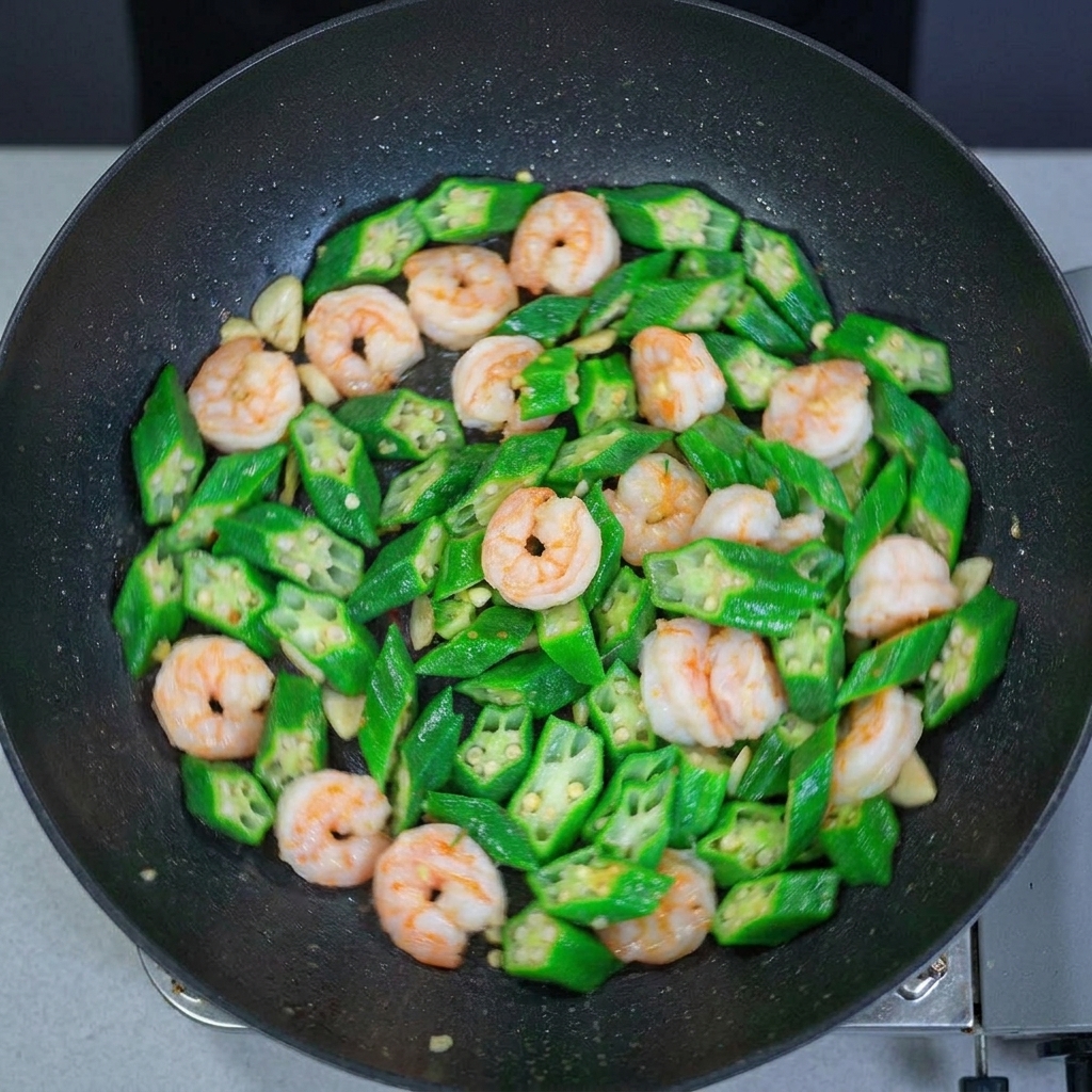 A top-down view of a wok filled with stir-fried okra and shrimp, showing the glossy finish and well-distributed ingredients.