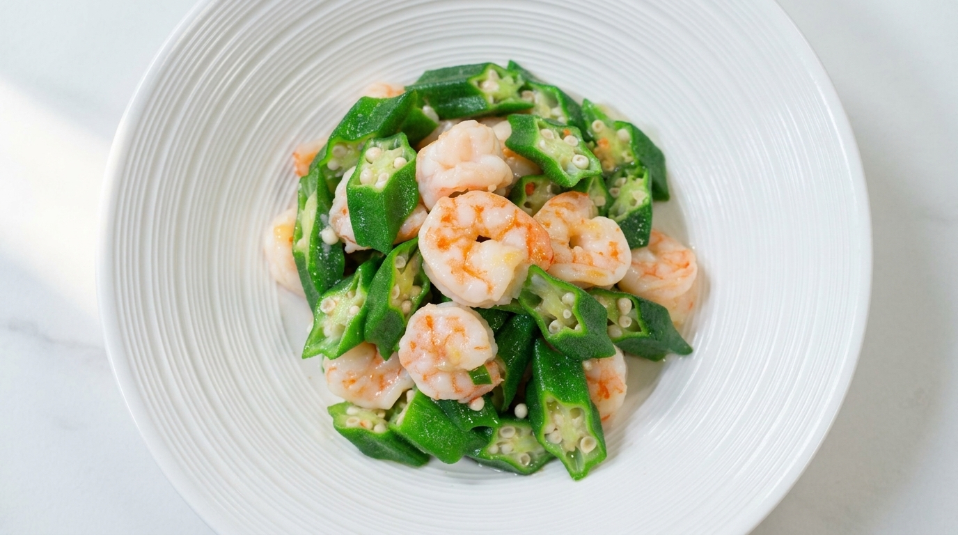Stir-fried okra and plump shrimp served in a white bowl, showing bright green colors and a light glossy glaze