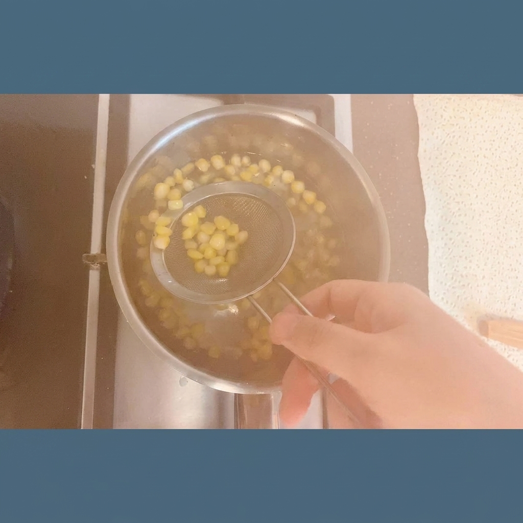 Bright yellow corn kernels being lifted out of a steaming pot of water with a stainless steel mesh strainer.