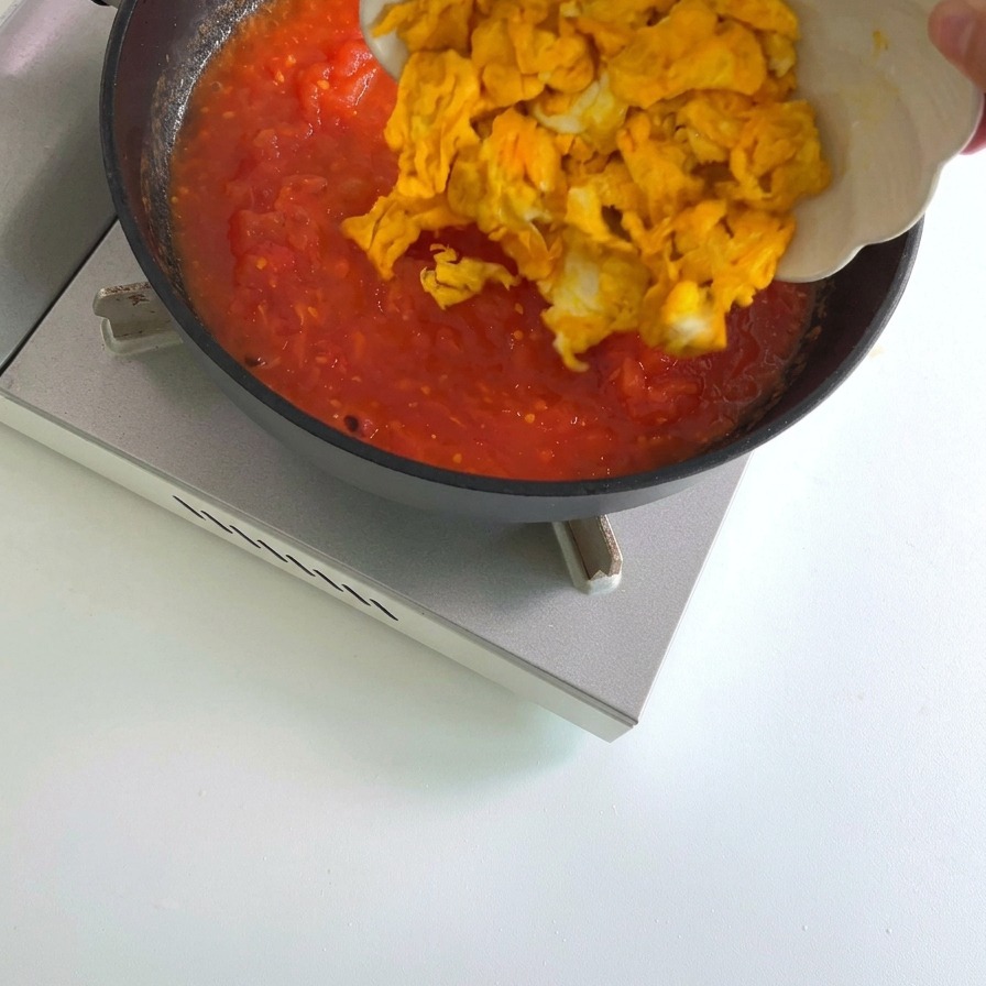 Cooked yellow scrambled egg pieces being added to a pan containing a simmering red tomato sauce.