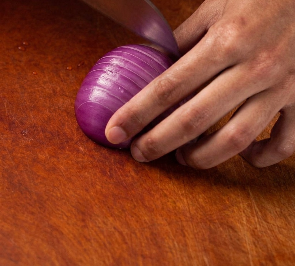 A sharp knife dicing a purple onion into fine, uniform cubes on a wooden cutting board.