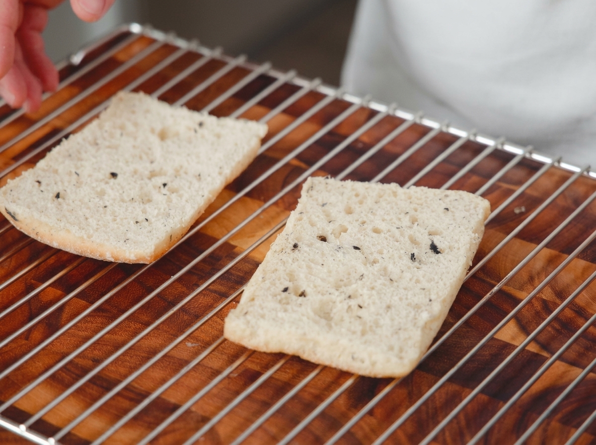 Two halves of sliced bread resting on a wire oven rack over a wooden surface, ready to be toasted.