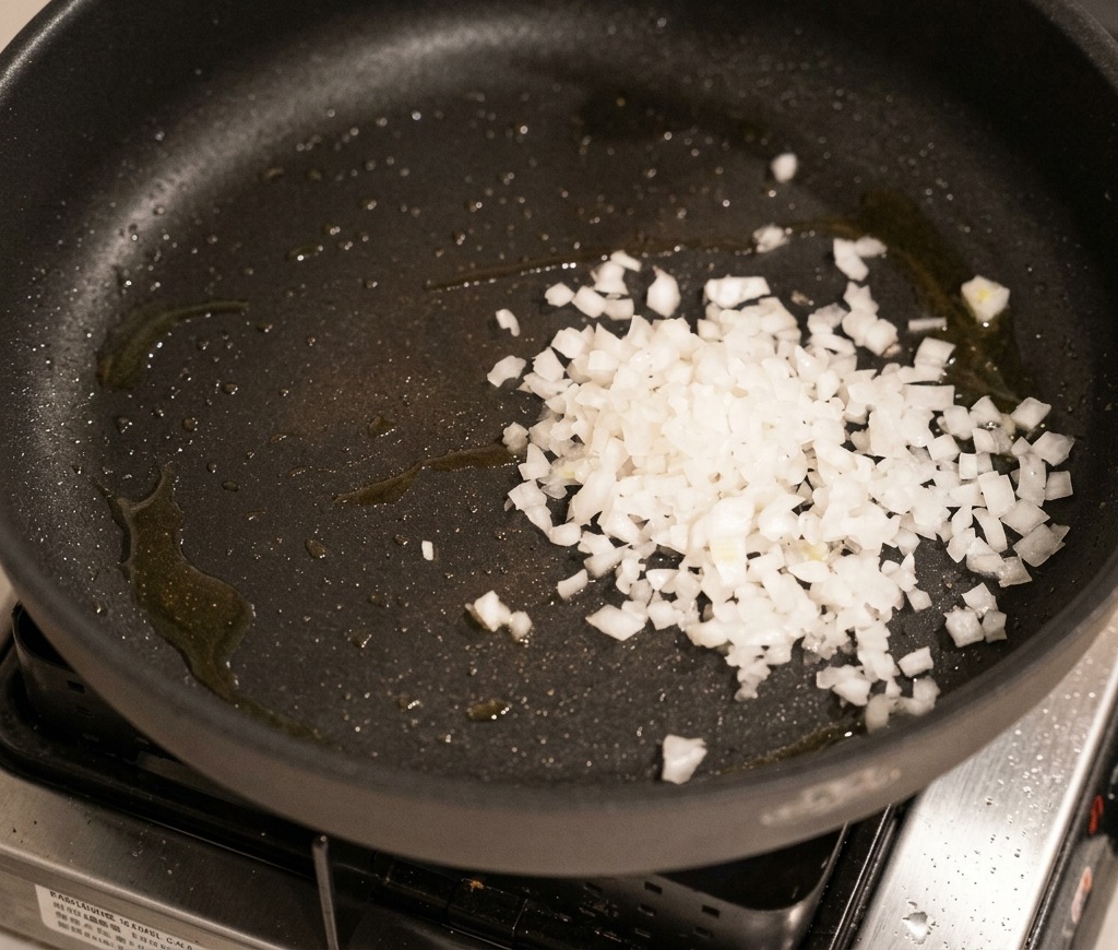 Diced white onions being sautéed in a dark pan until translucent and soft.