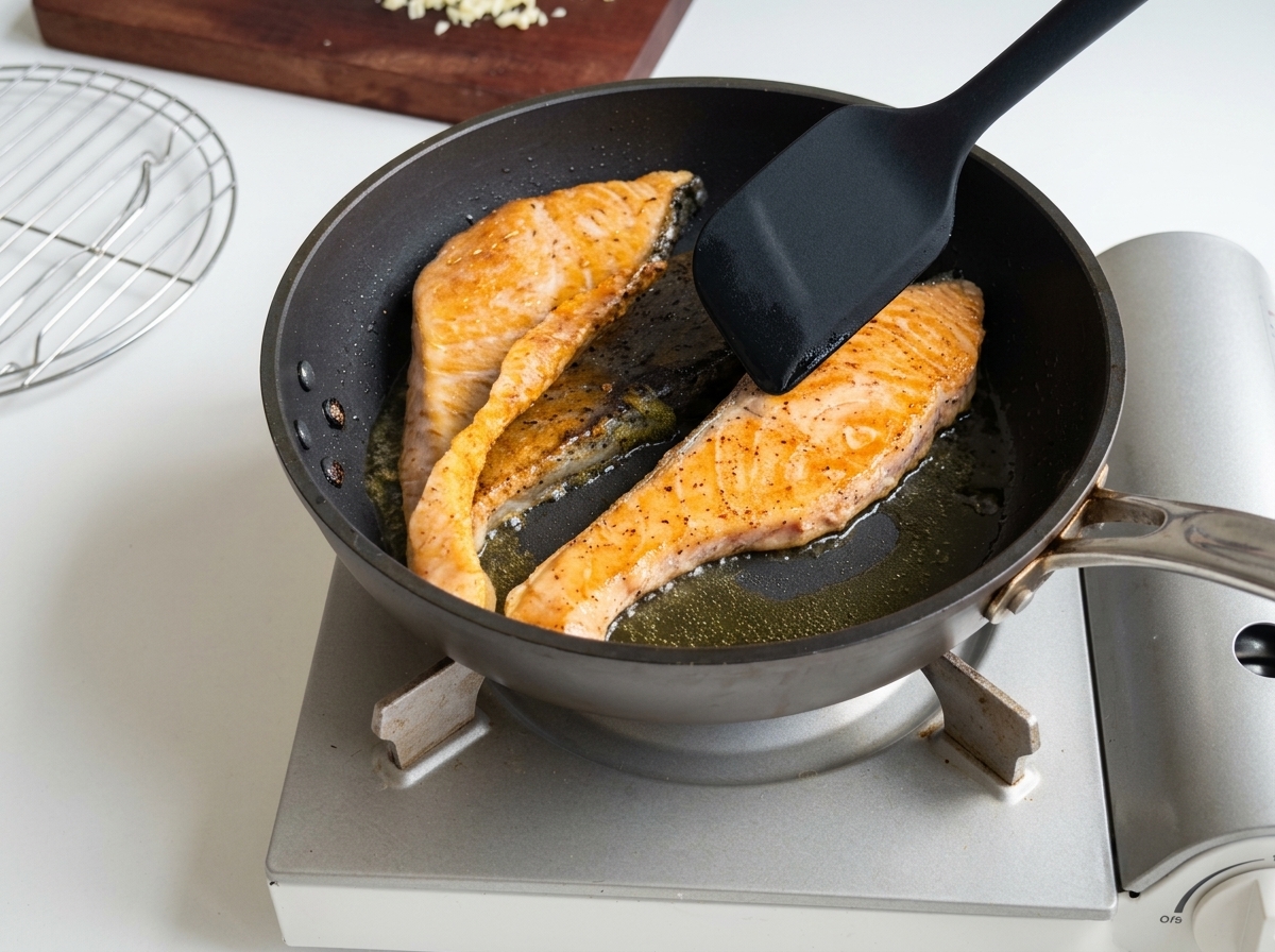 Salmon fillets being pan-seared in a skillet, showing golden-brown cooked surfaces and crispy skin.