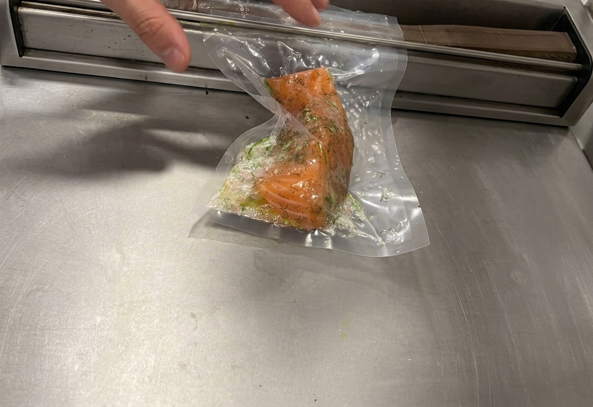 A vacuum sealing machine removing air from a plastic bag containing a herb-crusted salmon fillet.