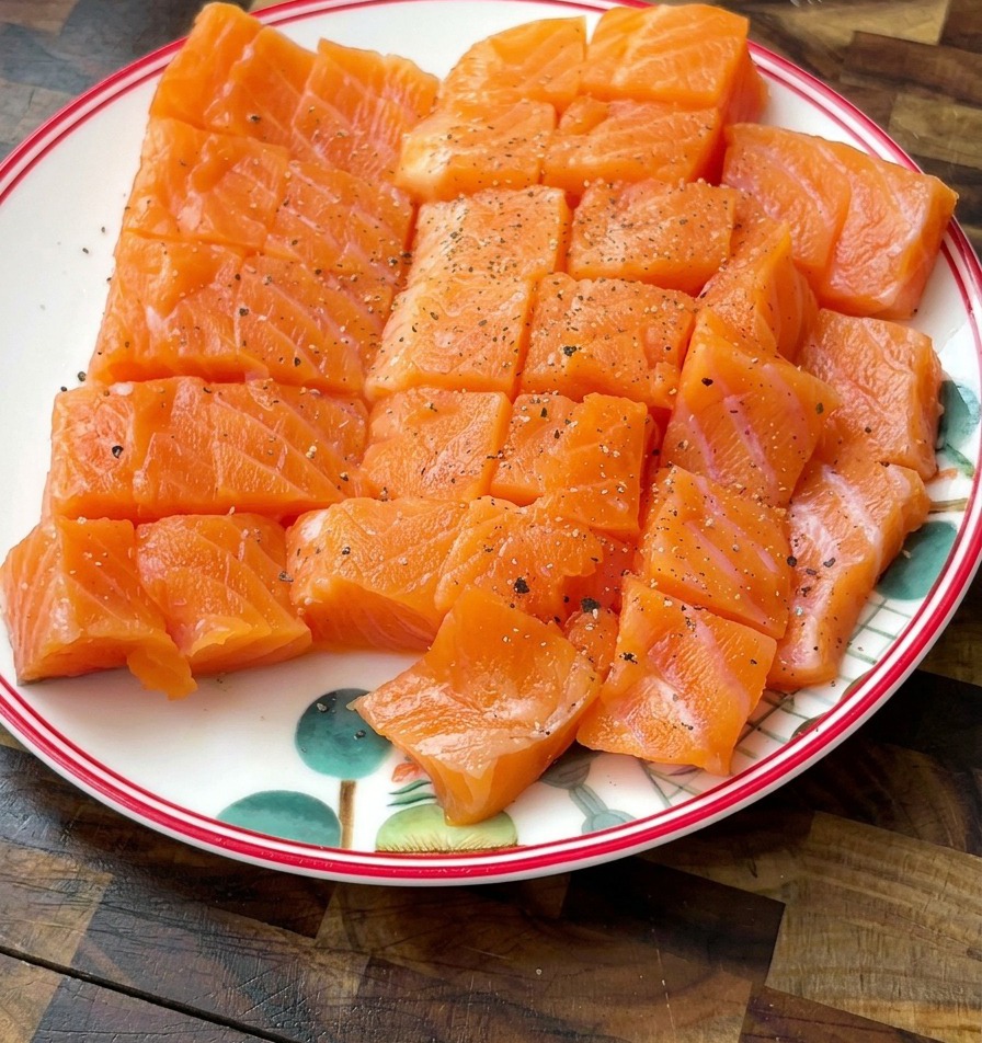 Diced salmon cubes on a white plate with visible specks of black pepper and salt seasoning.