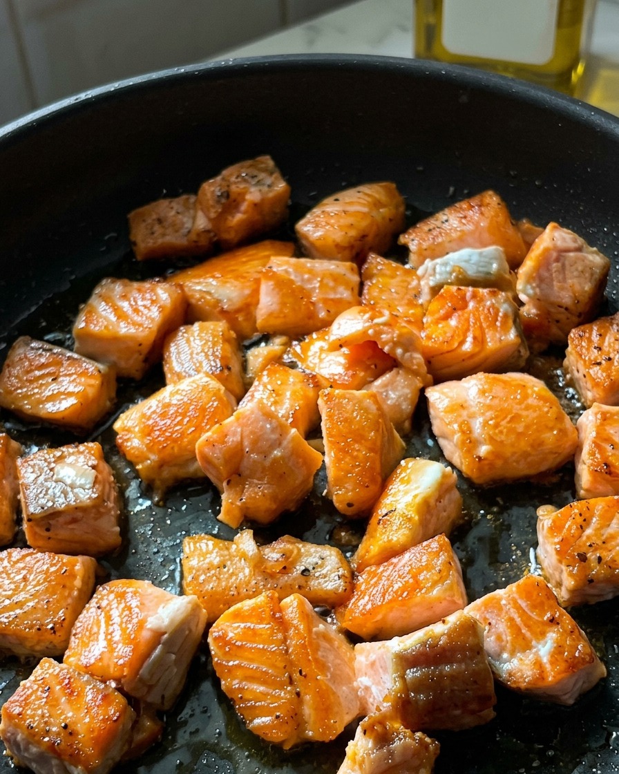 Cubed salmon pieces in a skillet with a crisp, golden-brown crust on their seared surfaces.